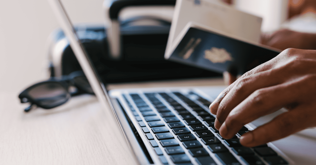 Traveller using a laptop with a passport and luggage beside them