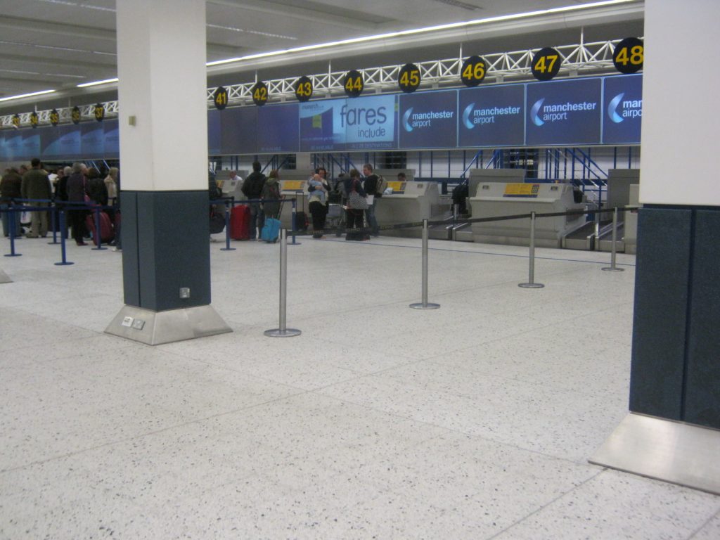 Passengers at check-in desks in a UK airport terminal
