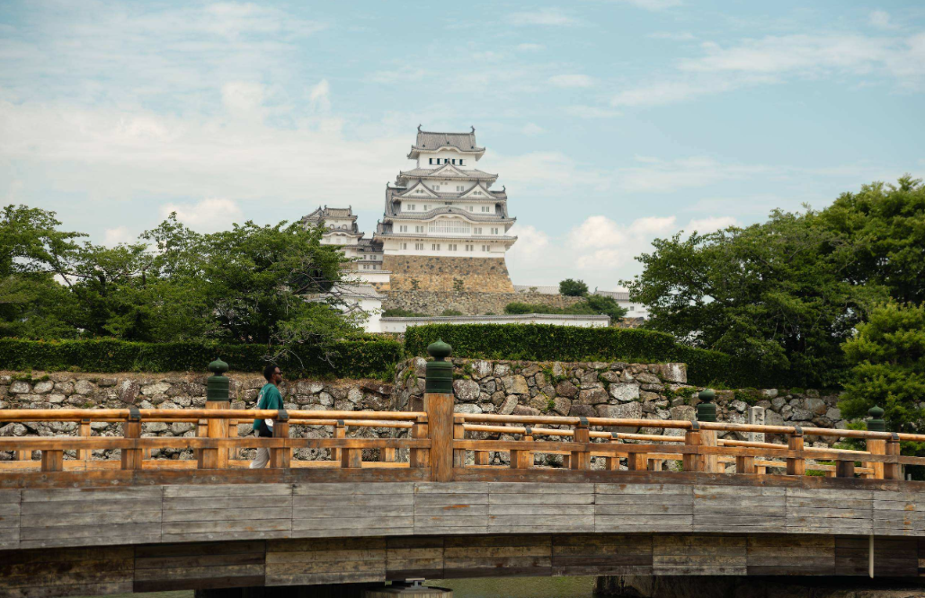 Visitor walking across a wooden bridge in front of a white castle in Hyogo, Japan